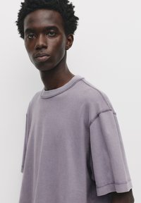 Lyslilla oversized t-shirt med korte ærmer, der har en rund halsudskæring og synlige syninger, vist på en neutral baggrund.
