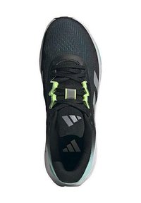 Zapatilla deportiva negra con parte superior texturizada, detalles en verde y suela blanca. Presenta cordones y una lengüeta acolchada con el detalle del logo.