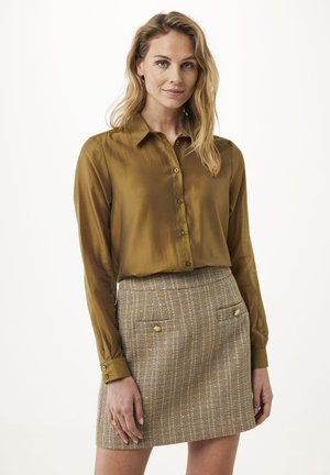 Olijfgroene satijnen shirt met kraag en knoopsluiting, gecombineerd met een gemêleerde geruite minirok met gouden knopen en zakken.