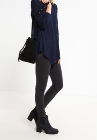 Marineblauw shirt met lange mouwen, zwarte skinny jeans, zwarte enkellaarsjes met een chunky hak, en een kleine zwarte handtas met trekkoord.