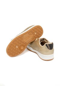 Baskets de sport beiges avec une semelle en caoutchouc beige, des détails texturés et une accentuation sombre au niveau du talon. Bout arrondi et design à lacets.