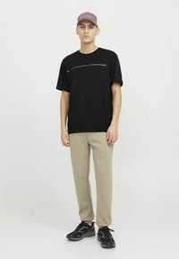 Sort crew-neck t-shirt med en vandret designlinje, parret med lyse beige tætsiddende bukser og sorte atletiske sko. Lys lilla cap bæres.