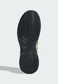 Czarna gumowa podeszwa buta z wzorem w zygzak, z wyraźnym logo Adidas i zielonym akcentem po boku dla lepszej widoczności.