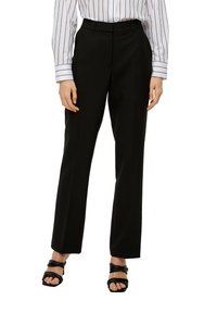 Zwarte, op maat gemaakte broek met een slim fit en persvouwen, gemaakt van een gladde stof. Gecombineerd met een wit gestreept shirt en zwarte sandalen met banden.