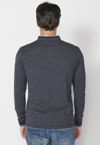 Polo majica dugih rukava u mornarskoplavoj boji s teksturiranom tkaninom i bijelim šavovima. Ima uski ovratnik i prilagođen dizajn na leđima.