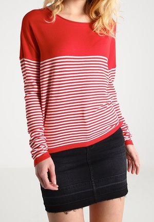 Femme portant un pull à manches longues rayé rouge et blanc associé à une jupe en jean noire avec un ourlet effiloché.