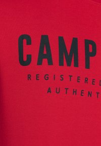 Red cotton t-shirt featuring bold black text that reads "CAMP" and smaller text that says "REGISTERED AUTHENTIC." Soft texture.