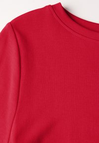 Punainen puuvillapaita, jossa on ribbitekstuuri ja klassinen pyöreä pääntie. Sileä kangas, istuva tyyli, ei näkyviä kuvioita tai yksityiskohtia.