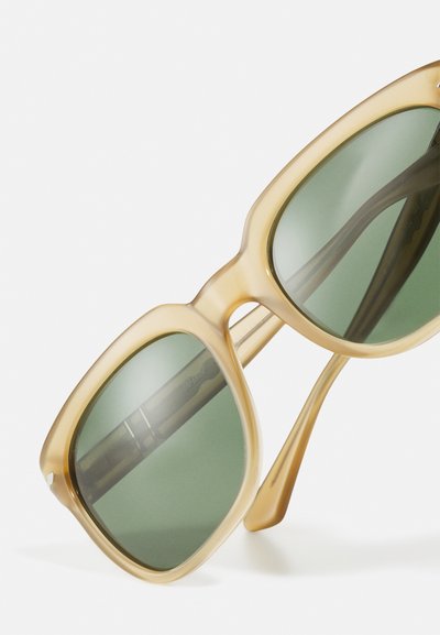 Óculos de sol de tom claro com armação oversized e arredondada, com lentes verdes. Hastes transparentes e textura suave em todo o design.