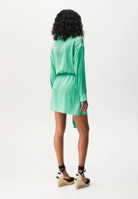 Abito camicia di satin verde menta con maniche lunghe, vita cinturata e orlo curvo. Abbinato a zeppe in espadrilles nere con lacci alla caviglia.