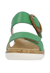 Sandales en cuir vert avec deux sangles croisées, une boucle ronde marron et une semelle texturée en liège. Design à bout ouvert avec une couverture minimale.