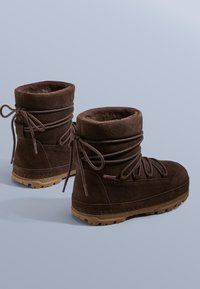 Barna bőrbarna bokacsizma puha, szőrmebéléssel, kerek orral és fűzős elemmel. Gumi talppal rendelkezik, amely texturált tapadást biztosít.
