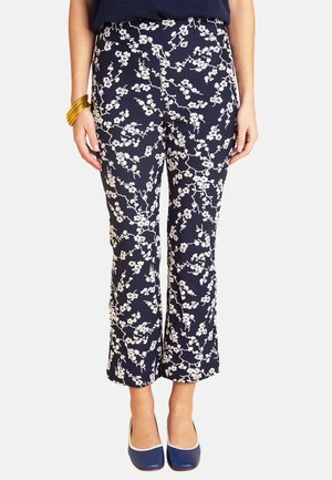 Woman wearing navy blue cropped pants with white floral print, navy shoes with white trim, and gold bangles on left wrist.