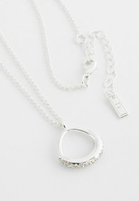 Collier en argent avec un pendentif en boucle comportant une rangée de petits cristaux transparents, attaché à une fine chaîne avec un fermoir à homard et une extension.
