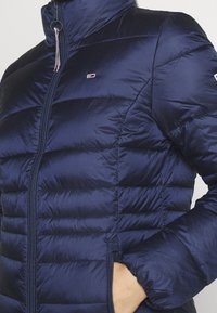Giacca imbottita blu navy con collo alto, chiusura frontale con cerniera e design trapuntato. Presenta una toppa con logo e polsini elastici per una vestibilità aderente.