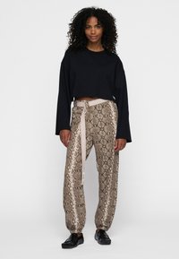 Sort cropped sweatshirt parret med beige bukser med slange mønster og et matchende bælte. Bukserne har en elastisk manchet ved anklen.