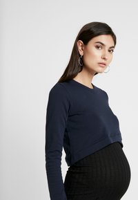 Top de manga longa cropped azul marinho feito de algodão, combinado com uma saia preta canelada. O top apresenta um decote redondo e mangas justas.