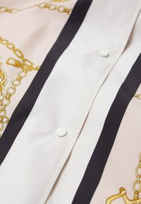Koszula z kołnierzykiem o jedwabistej fakturze, jasnoróżowe tło, czarne paski i wzór ze złotym łańcuszkiem; z białymi guzikami z przodu.