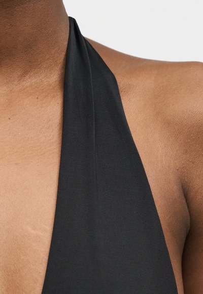 Κοντινό πλάνο στον λαιμό και τον ώμο ενός ατόμου που φορά μαύρο τοπ χωρίς μπράτσα με απαλή υφή, πάνω σε φωτεινό φόντο.