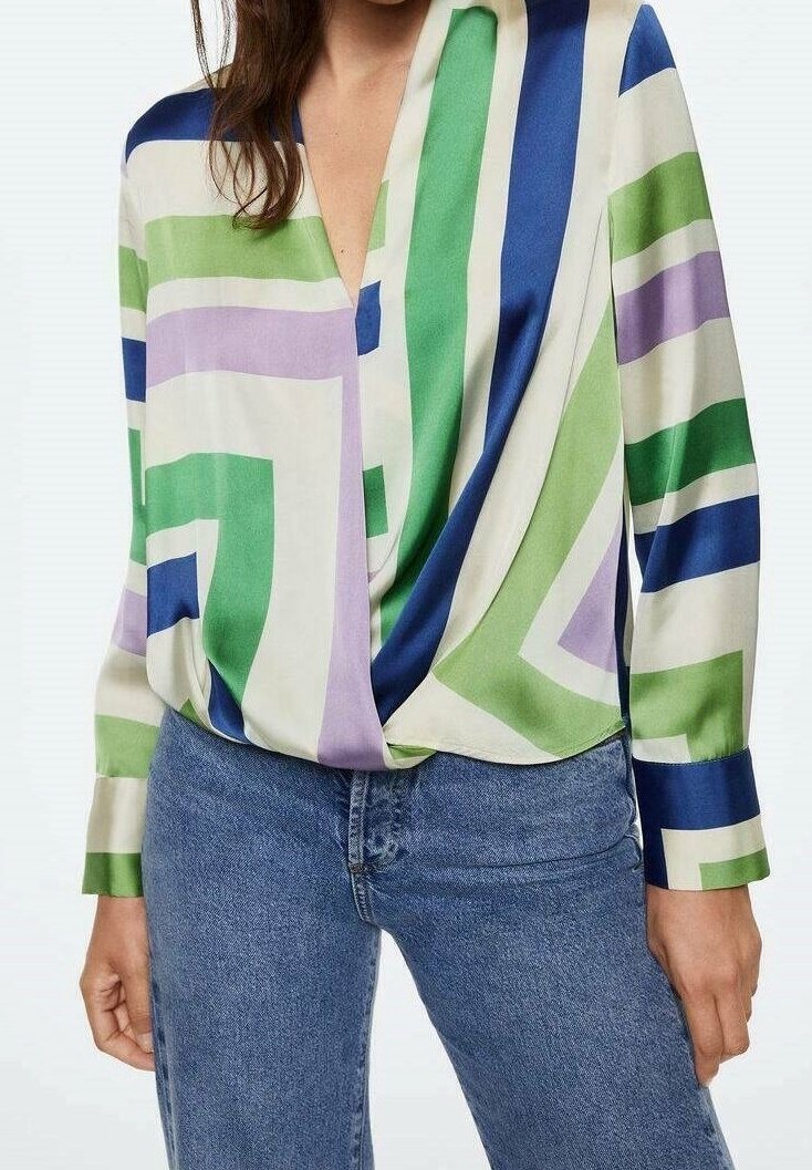 Blusa in seta con un motivo geometrico nei toni del verde, blu e viola, caratterizzata da una profonda scollatura a V e dettagli drappeggiati sul davanti. Abbinata a dei jeans.