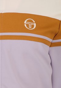 Short-sleeve shirt featuring a lavender base with orange and white horizontal stripes. Includes a circular logo in white on the chest.
