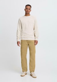 Beige textured sweatshirt with a round neckline, paired with khaki trousers. Footwear features white and brown stripes. Simple design.