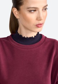 Bordeaux sweatshirt met ronde hals, gedragen over een marineblauwe ribgebreide coltrui met een gerimpelde rand. Soepele textuur en casual ontwerp.