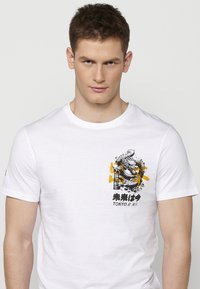 White cotton t-shirt featuring a graphic print of a dragon in black and yellow with Japanese text and accents on the chest area.