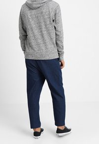 Sudadera gris de punto con capucha ajustable. Combinada con pantalones sueltos de color azul oscuro y zapatillas negras con detalles en blanco.