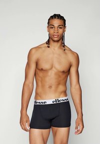 Schwarze Boxershorts mit einem weißen elastischen Bund, der das "ellesse"-Logo trägt. Glattes Material, enganliegendes Design, mittellange Beine bis zur Mitte des Oberschenkels.