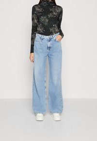 Svart långärmad topp med ett stjärnmönster, kombinerad med ljusblå vida jeans och vita sneakers. Outfiten har en avslappnad passform och ett ledigt design.