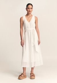 Balta, be rankovių suknelė su V formos iškirpte, akių raštu ir audinio diržu. Derinama su rudomis, platformos basutėmis, turinčiomis dvigubo dirželio dizainą.