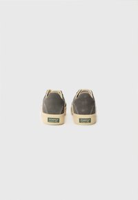 Baskets en daim gris avec des semelles en caoutchouc beige contrastantes. Présente un patch logo vert sur le talon et un design simple avec un système de laçage.