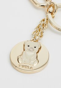Portachiavi dorato con un disco tondo caratterizzato da un design dettagliato di un orso in rilievo e la parola "Furla" incisa sotto. I link della catena sono lucidi e testurizzati.