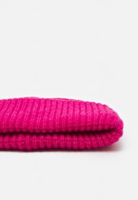 Écharpe en laine rose tricotée, pliée, présente une texture côtelée avec une finition douce. Aucun élément de quincaillerie ou motif présent.
