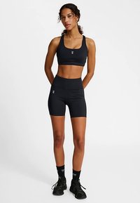 Czarny sportowy biustonosz i spodenki z wysokim stanem, wykonane z elastycznego materiału. Charakteryzują się smukłym designem z subtelnymi akcentami logo. Czarny obuwie i skarpetki.