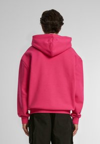 Sudadera con capucha rosa de corte holgado, con puños y dobladillo acanalados. Material suave, presenta una gran capucha y sin logotipos ni patrones visibles.