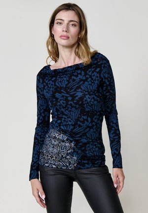 T-shirt à manches longues avec un motif floral bleu sur fond noir, accompagné d'une section texturée à motifs gris au niveau de la taille. Pantalon noir.