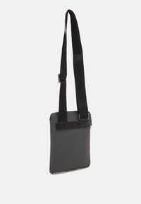 Borsa nera con una finitura opaca e texture, caratterizzata da una lunga tracolla regolabile e un design rettangolare semplice con chiusura superiore.
