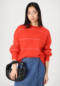 Red striped knit sweater made of soft yarn, featuring long sleeves. Paired with a blue denim skirt and a black faux leather handbag.