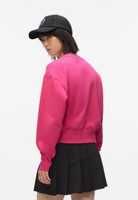 Felpa fucsia corta con maniche lunghe, polsini e orlo a coste, abbinata a una gonna plissettata nera e un berretto in rete nero.