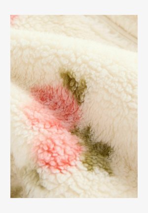 Pehmea, tekstureeritud tekk, millel on kreemjas alus ja roosa ning rohelise täppidega aktsendid, esitleb udupehmet ja kohevat materjali.