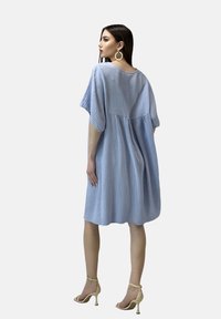 Vestido azul claro, a la altura de la rodilla, con mangas cortas, tejido texturizado y un corte relajado. Sutil fruncido en la cintura. Lleva unas sandalias de tacón nude.