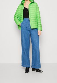 Gepadde groene jas met rits, zwart topje en wijde blauwe spijkerbroeken. Zwarte laarzen met hak maken de outfit compleet.