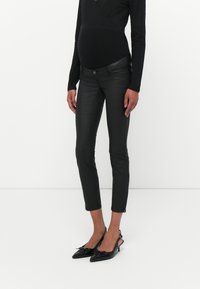 Zwarte nep leren broek met een slim fit, voorzien van een knoopsluiting en details met een zijrits, gecombineerd met zwarte puntige hakken.