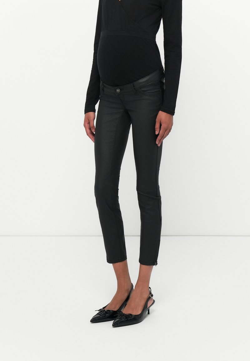 Schwarze Kunstlederhose mit schmaler Passform, mit einem Knopfverschluss und seitlichen Reißverschlussdetails, kombiniert mit schwarzen spitzen Pumps.