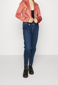 Červená motorkářská bunda z umělé kůže se zipovými kapsami, doplněná tmavě modrými džínami s vysokým pasem a černými robustními kotníkovými botami na platformě.