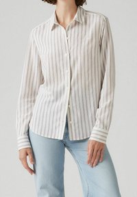 Chemise à boutons en tissu léger, présentant des rayures verticales rouges et bleues sur fond blanc. Manches longues avec des poignets rayés.