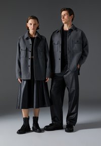 Grå uldjakker med store frontlommer, båret over en sort top og læderskørt. Sorte kampstøvler fuldender outfittet.