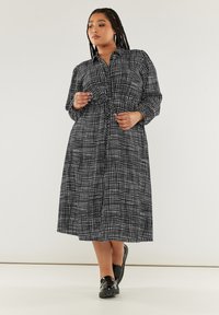 Svart och vit mönstrad maxiklänning med knäppning fram, långa ärmar och insnörning i midjan, med ett rutmönster och mjuk tyg.